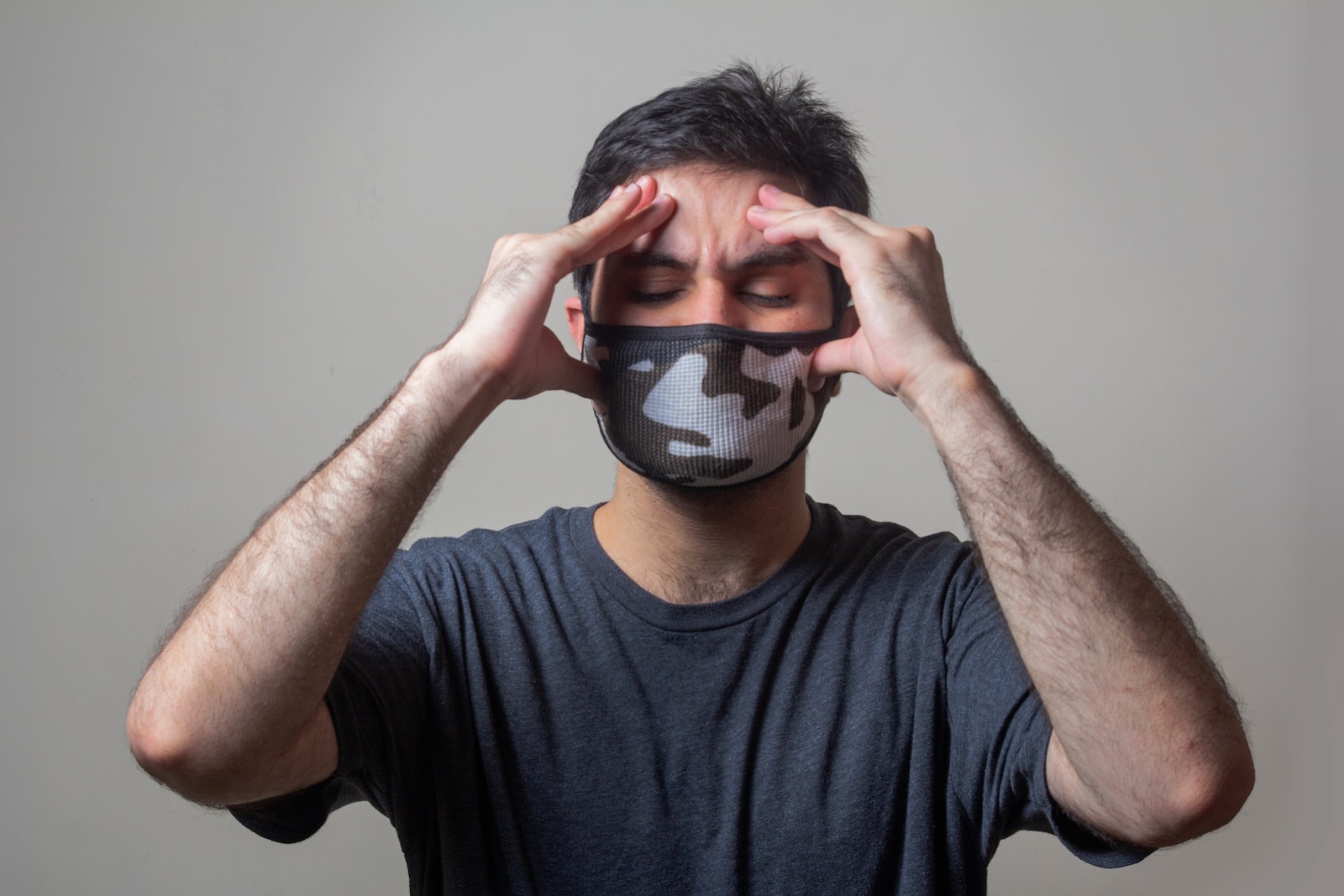 Maske takmış, elleriyle başını tutan yorgun görünümlü bir adam